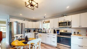 A modern kitchen with white cabinets, stainless steel appliances, and a wooden dining table. - Southbrook Cottage-Waterfront*Pet Friendly*A/C*Washer/Dryer (Greenville)