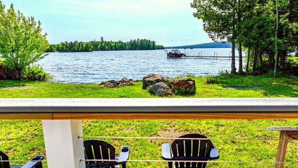 A lakeside view with two Adirondack chairs facing the water, a wooden deck, and a distant boat. - Southbrook Cottage-Waterfront*Pet Friendly*A/C*Washer/Dryer (Greenville)