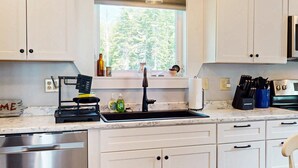 A kitchen with white cabinets, a stainless steel dishwasher, a sink with a black faucet, and a window above the sink. - Southbrook Cottage-Waterfront*Pet Friendly*A/C*Washer/Dryer (Greenville)