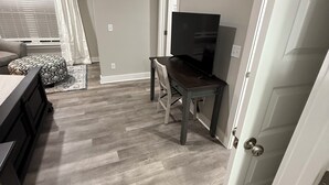Una habitación con cama, escritorio, televisor y puerta.