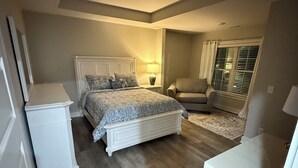 Un dormitorio con cama, mesita de noche, silla y una ventana con persianas.