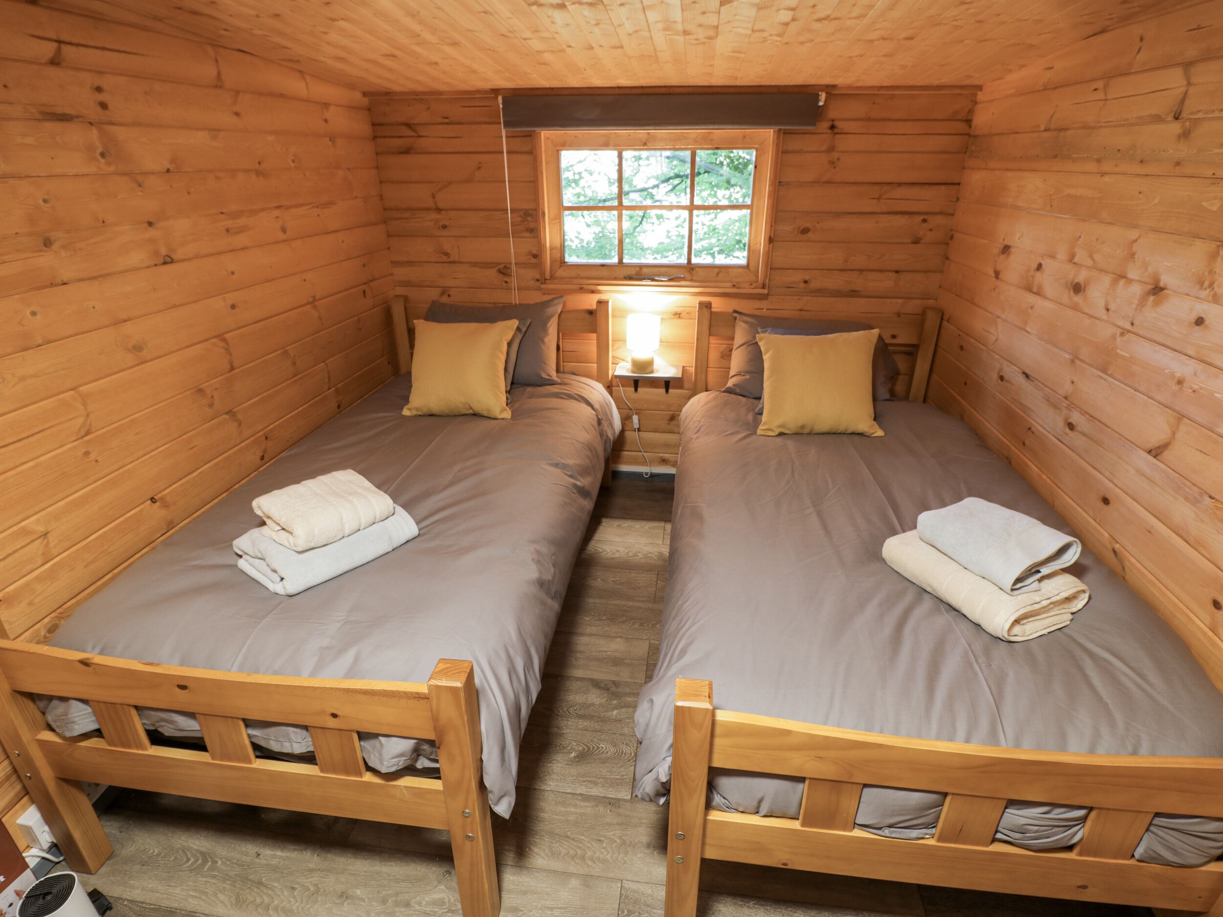 Pequeña y acogedora habitación tipo cabaña con dos camas de madera, cada una con una almohada y una toalla doblada.