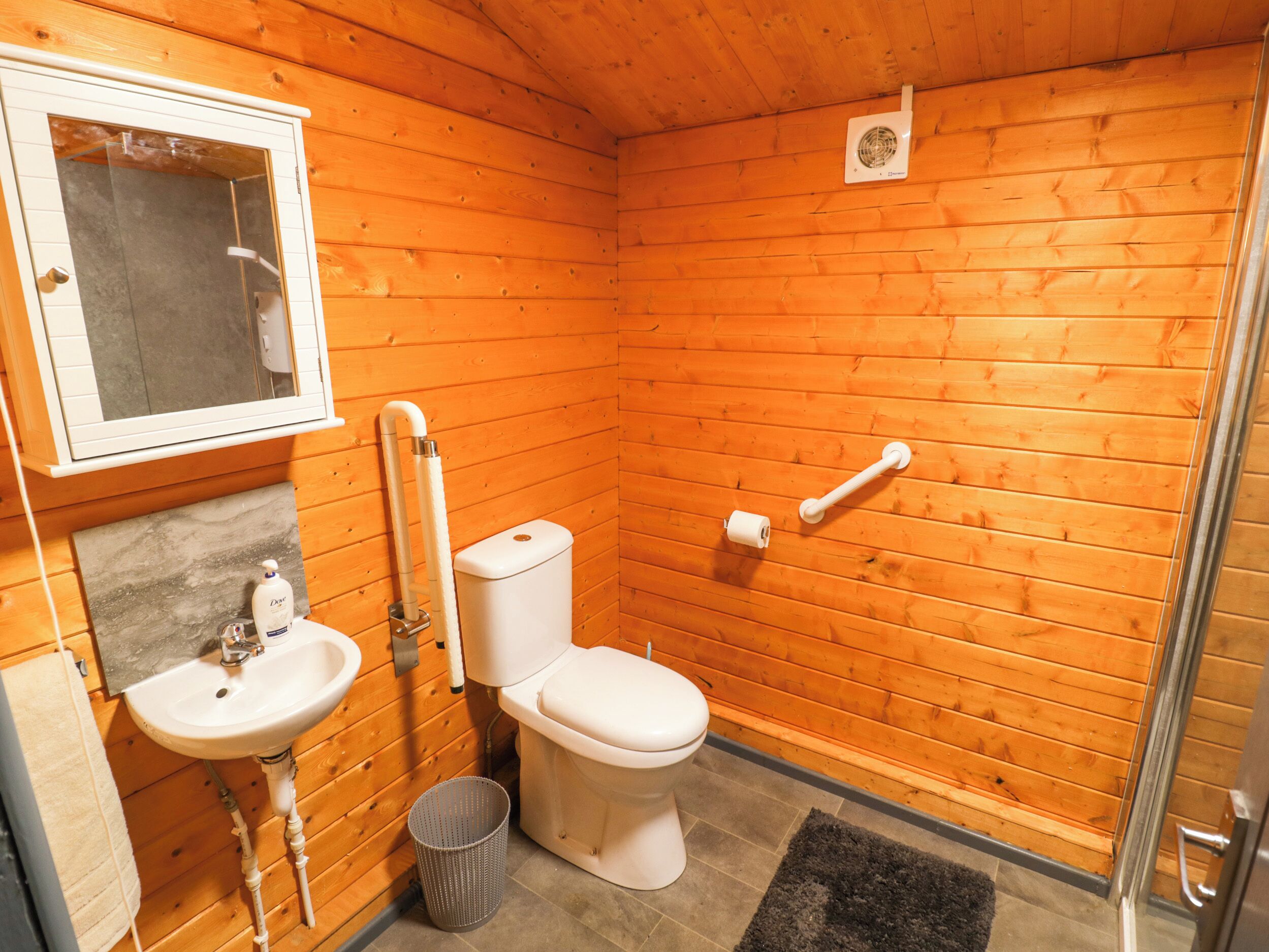 A small, wooden-paneled bathroom with a sink, toilet, and shower.
