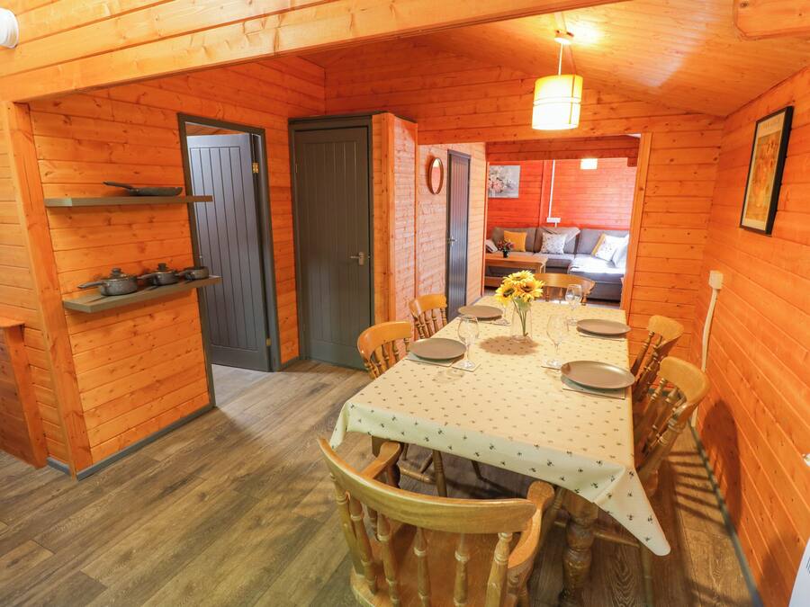 A wooden interior with a dining table set for four, a sofa, and a kitchen area with pots on the wall.