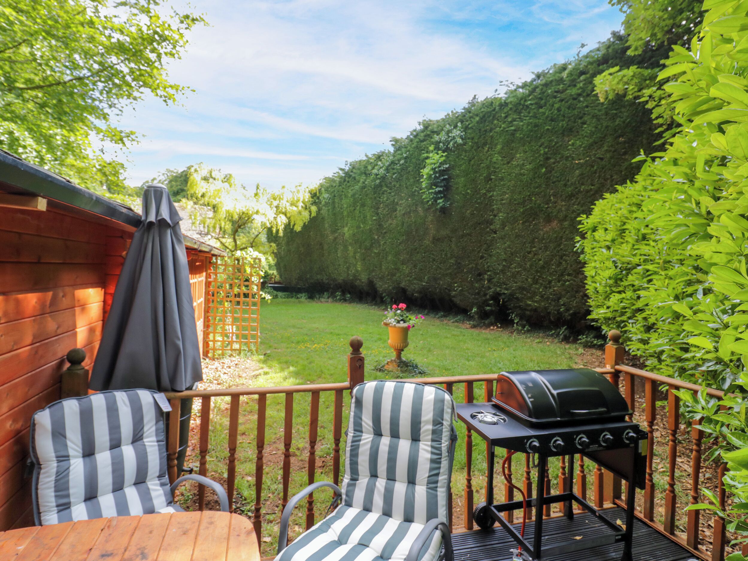 Une terrasse en bois avec deux chaises à rayures, un barbecue et une plante en pot.