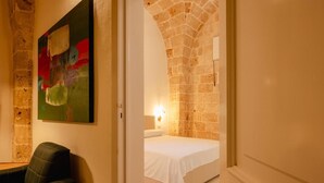 A bedroom with a stone archway, a bed, a nightstand, and a painting on the wall. - Le Casine di Maruggio 9 (Maruggio)