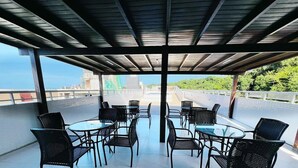 Un espacio al aire libre con mesas y sillas, con vista a un paisaje urbano y zonas verdes.