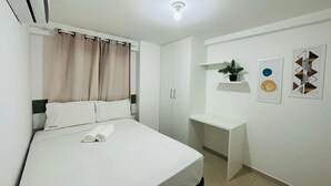 Habitación de hotel ordenada con una cama, un escritorio y una estantería con una planta.