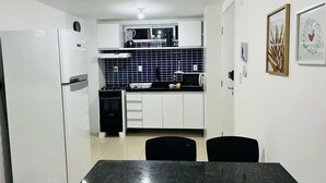 Una cocina compacta con armarios blancos, encimera negra y comedor con mesa y sillas negras.