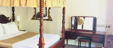 Una cama con dosel, un escritorio de madera, una silla y un espejo.