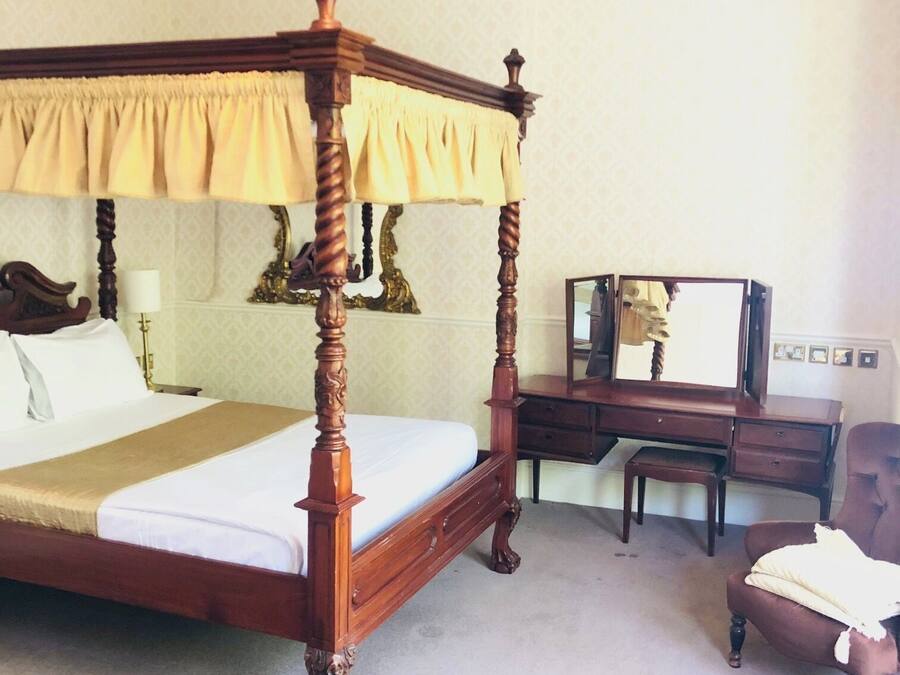 Een hemelbed met baldakijn, een houten bureau, een stoel en een spiegel.