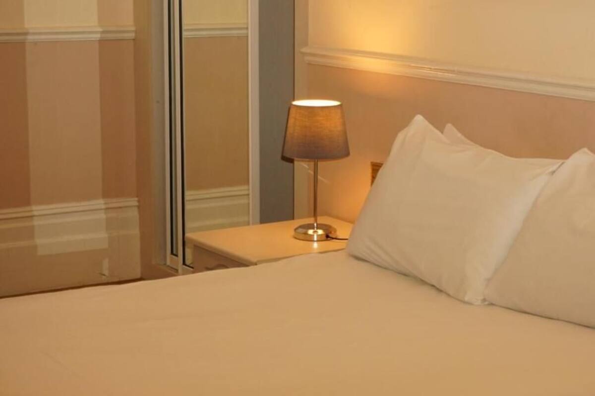 A hotel room with a bed, a nightstand, and a lamp.