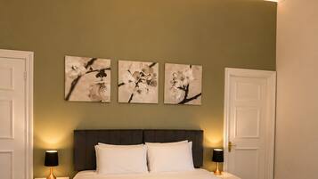 A hotel room with a bed, two bedside tables, a chandelier, and three wall-mounted flower paintings.