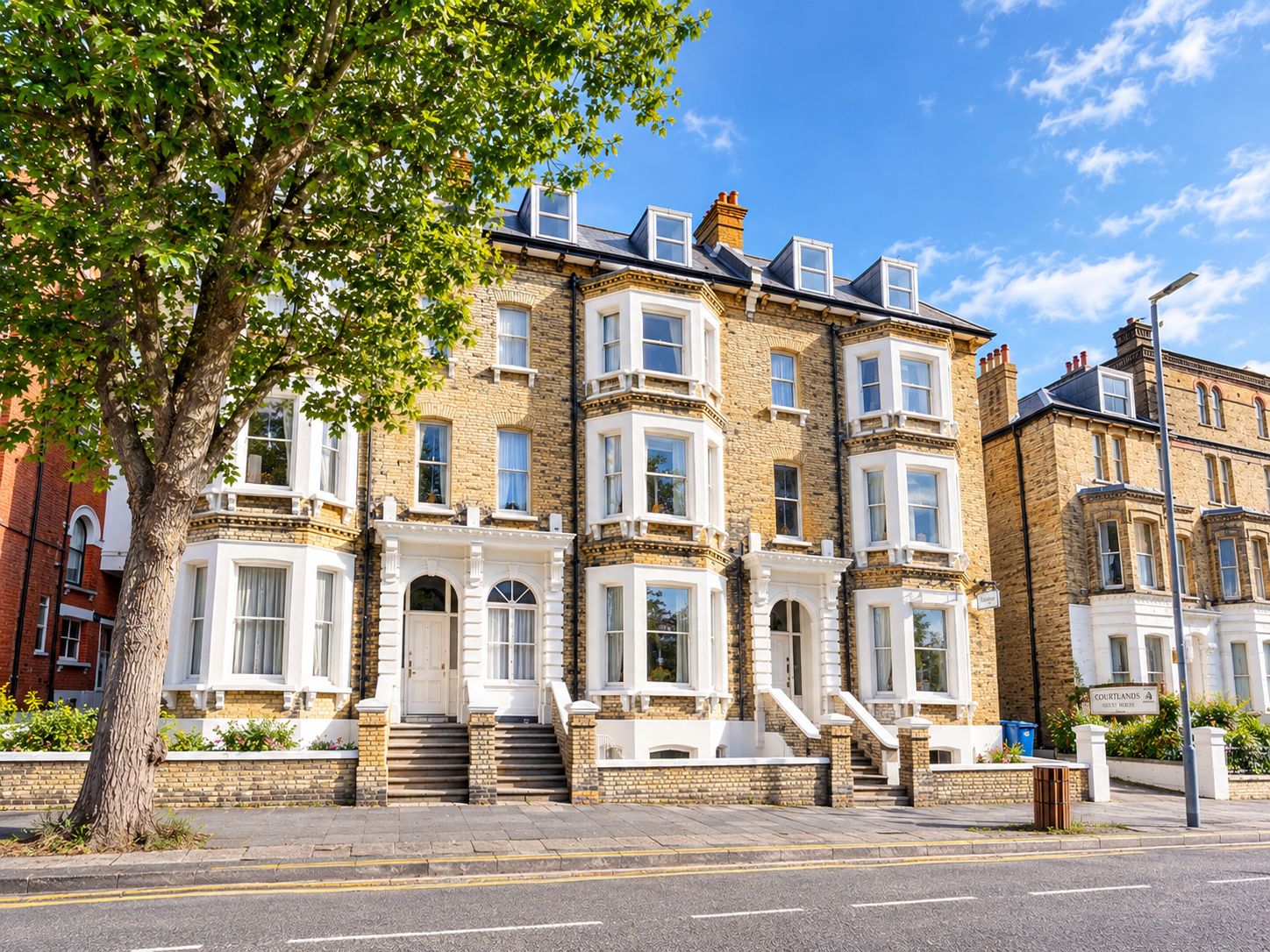 A row of terraced houses with a central entrance, a tree in the foreground, and a clear sky.