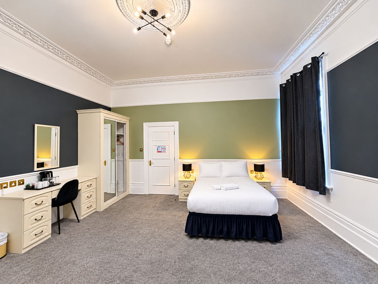 A hotel room with a bed, a desk, a chair, a wardrobe, and a mirror.