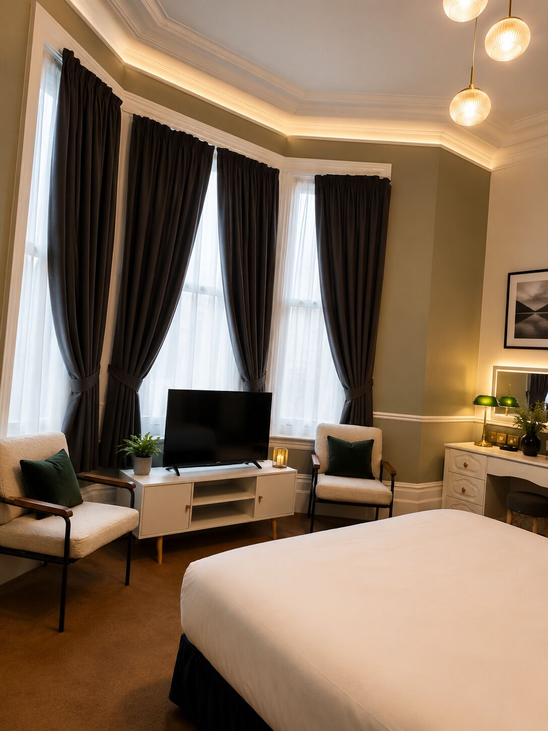 Une chambre d’hôtel avec un lit, un bureau avec une télévision, deux chaises et une lampe de bureau.