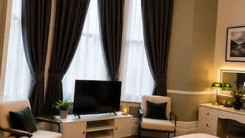 A hotel room with a bed, a desk with a TV, two chairs, and a desk lamp.
