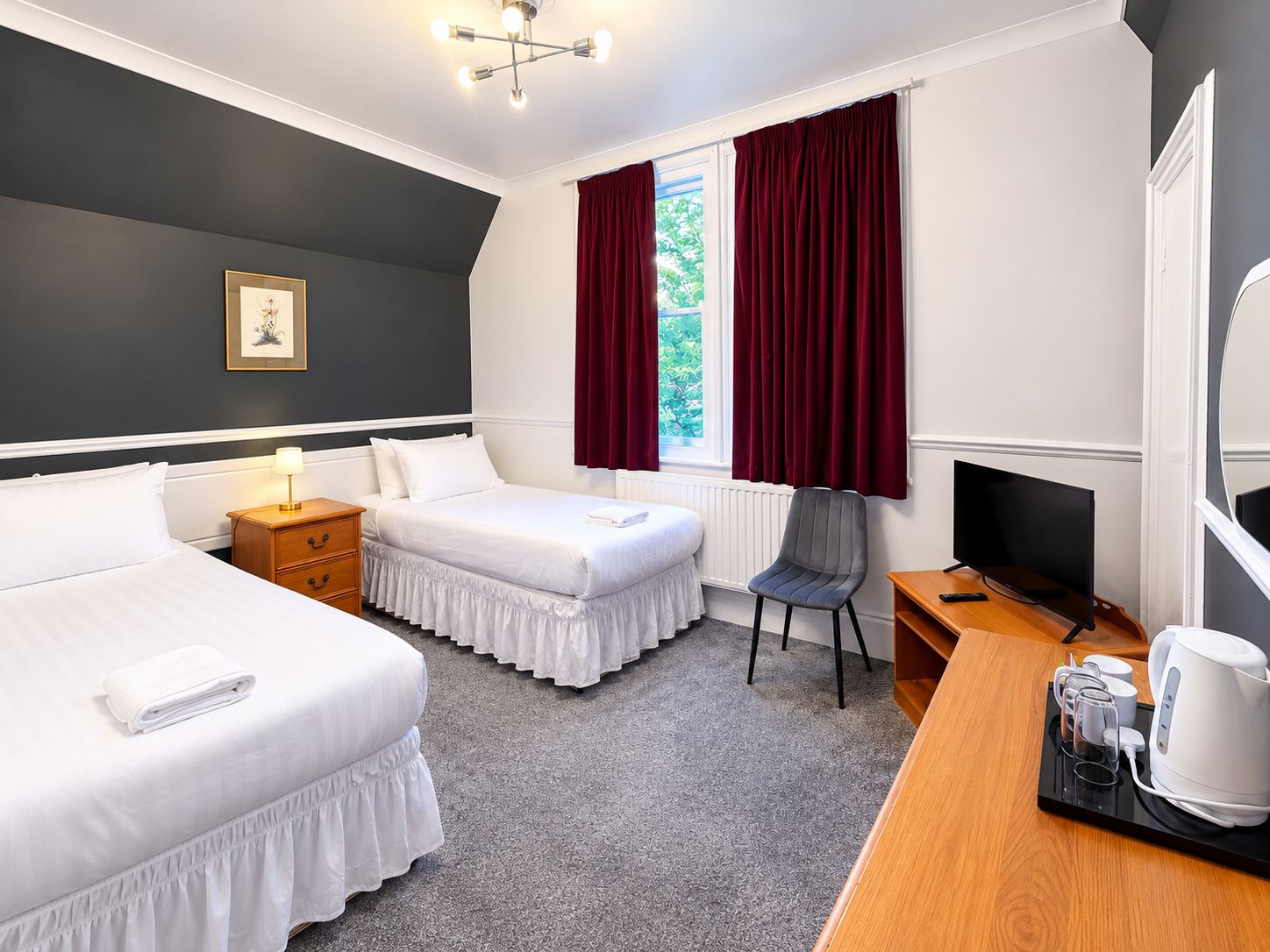 A hotel room with two beds, a desk with a television, a chair, and a coffee maker.