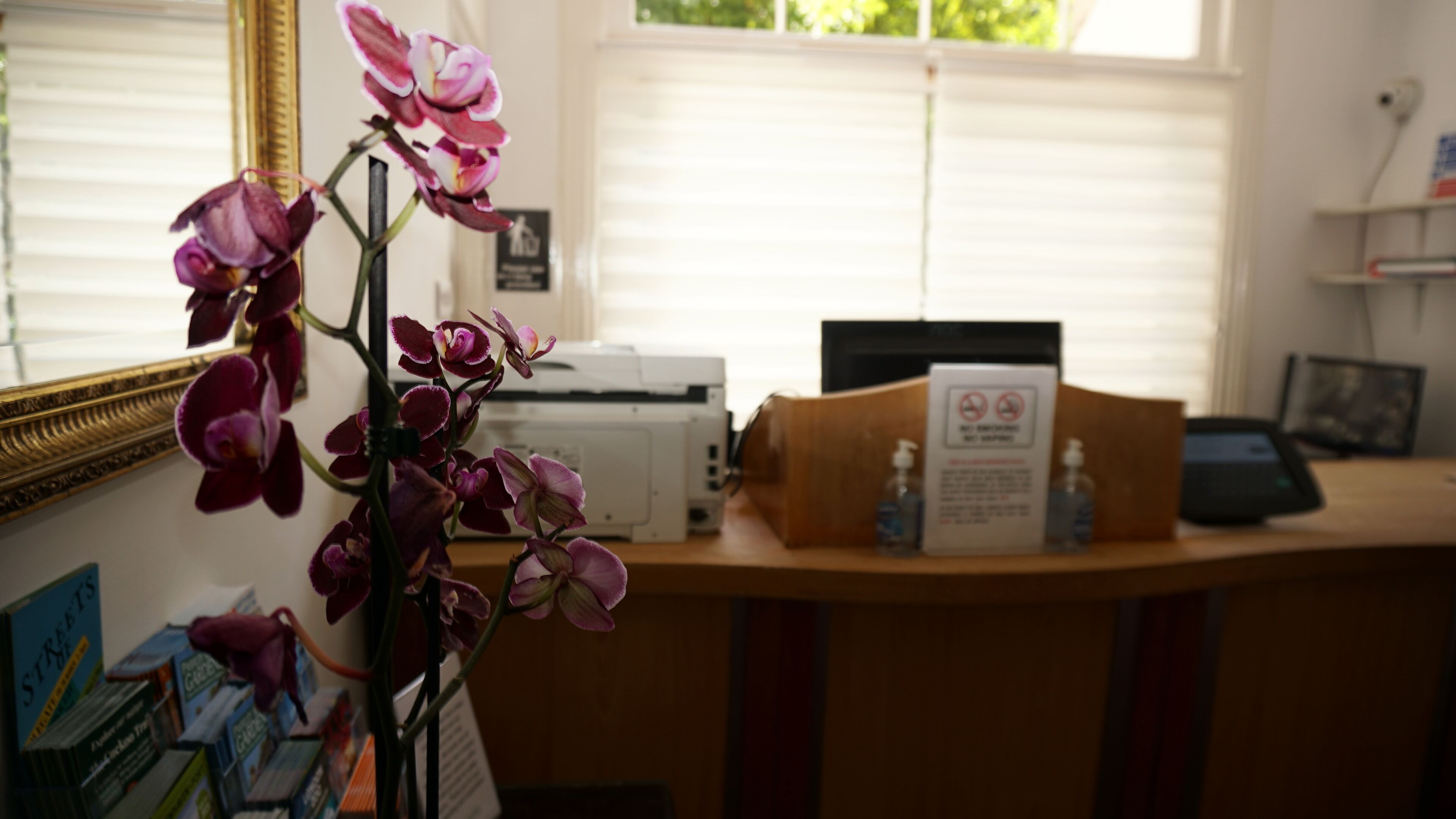 A desk with a printer, a sign about no smoking, and a bottle of hand sanitizer.