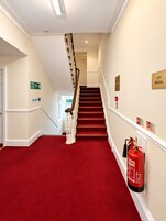 Un pasillo de hotel con alfombra roja, una escalera y un letrero de salida de incendios.