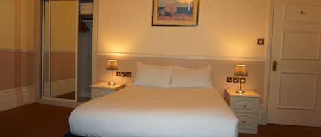 Habitación de hotel con una cama, dos mesitas de noche con lámparas, una puerta, un espejo y un cuadro en la pared.