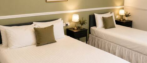 A hotel room with two beds, a framed botanical print on the wall, bedside lamps, and a carpeted floor.