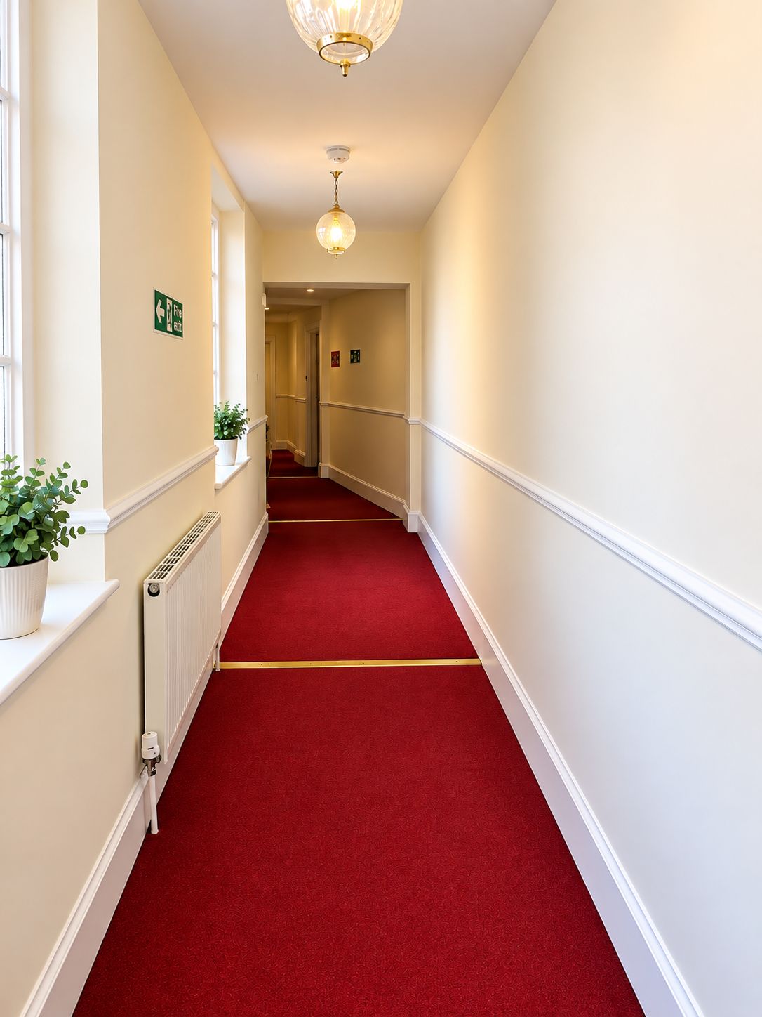 A hotel hallway with a red carpet, white walls, and a ceiling light fixture.