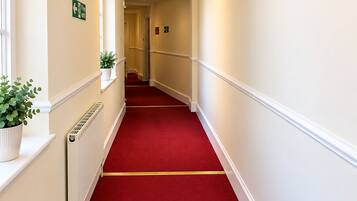 A hotel hallway with a red carpet, white walls, and a ceiling light fixture.