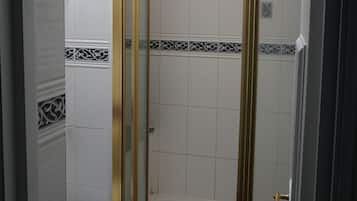 A bathroom with a white toilet, a shower with gold trim, and decorative tiles.