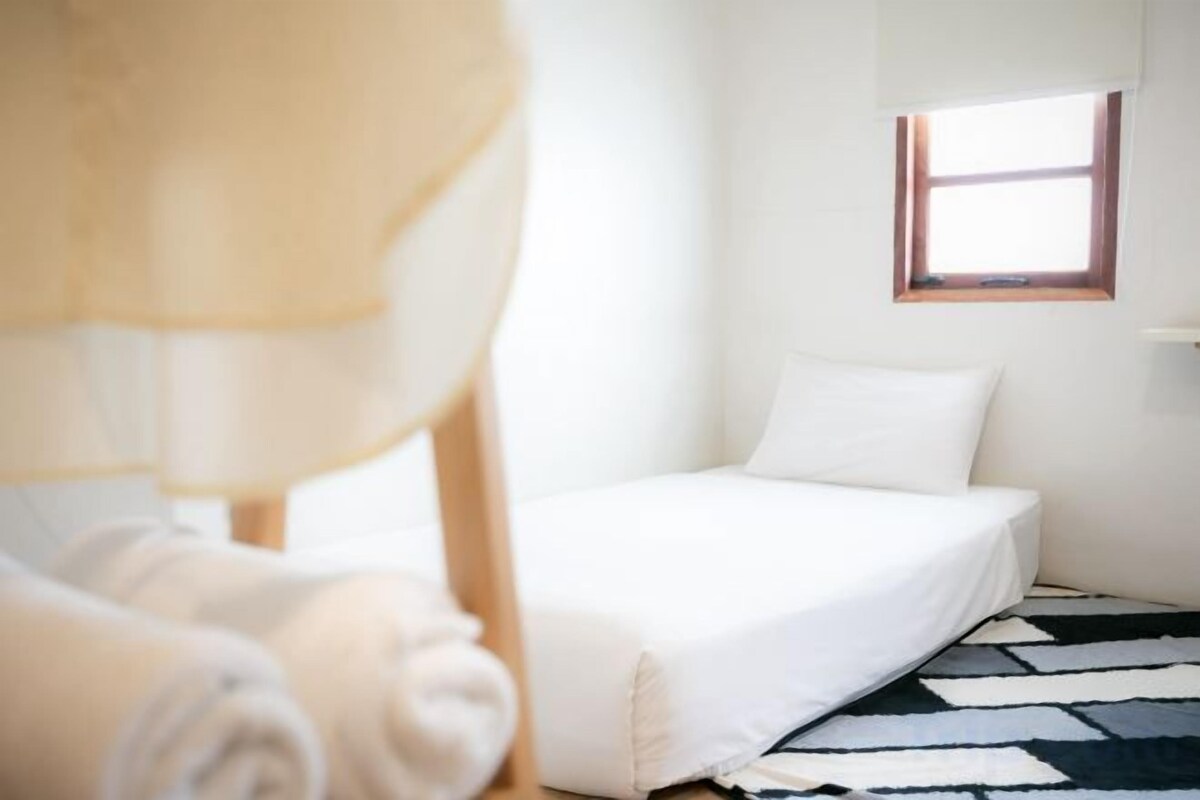 Un dormitorio con cama, ventana y una alfombra estampada.