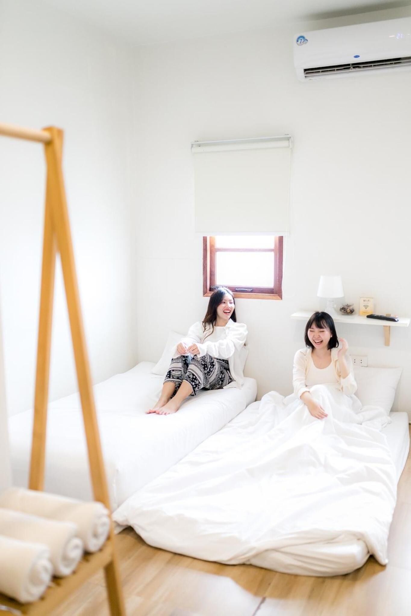 A minimalist room with two beds, a standing easel, and a window with blinds.