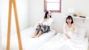 A minimalist room with two beds, a standing easel, and a window with blinds.