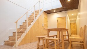 Una escalera con escalones de madera y barandillas blancas, puertas de madera, y una mesa con bancos en una habitación con paredes blancas y suelo de madera.