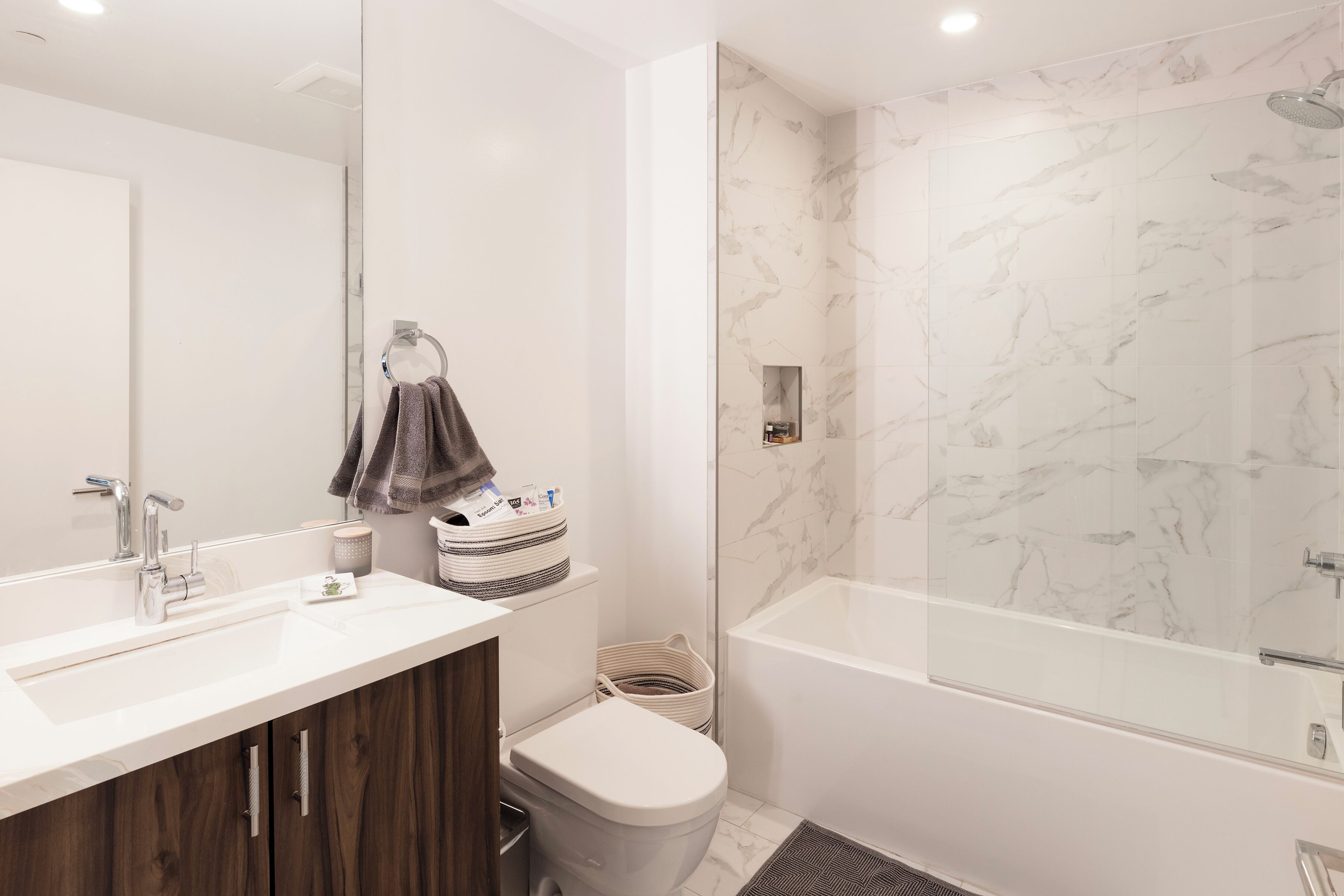 A modern bathroom with a marble shower, a white sink, and a wooden vanity.