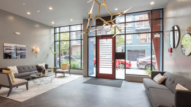 A modern lobby with a grey sofa, a coffee table, and a chair. There is a large window with a view of the street and parked cars. - Charming 1-bedroom condo in fabulous San Francisco with WiFi, AC fully furnished (San Francisco)