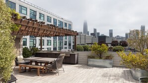 An outdoor patio with a pergola, seating, and a grill area, overlooking a cityscape with modern buildings. - Charming 1-bedroom condo in fabulous San Francisco with WiFi, AC fully furnished (San Francisco)