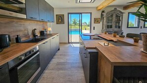 A modern kitchen with a built-in oven, a coffee machine, and a view of a pool through glass doors.