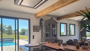 A modern kitchen with a large island, wooden beams, and a view of a swimming pool.