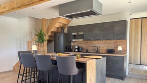 A modern kitchen with a central island, bar stools, a built-in oven, and a staircase leading to another level.