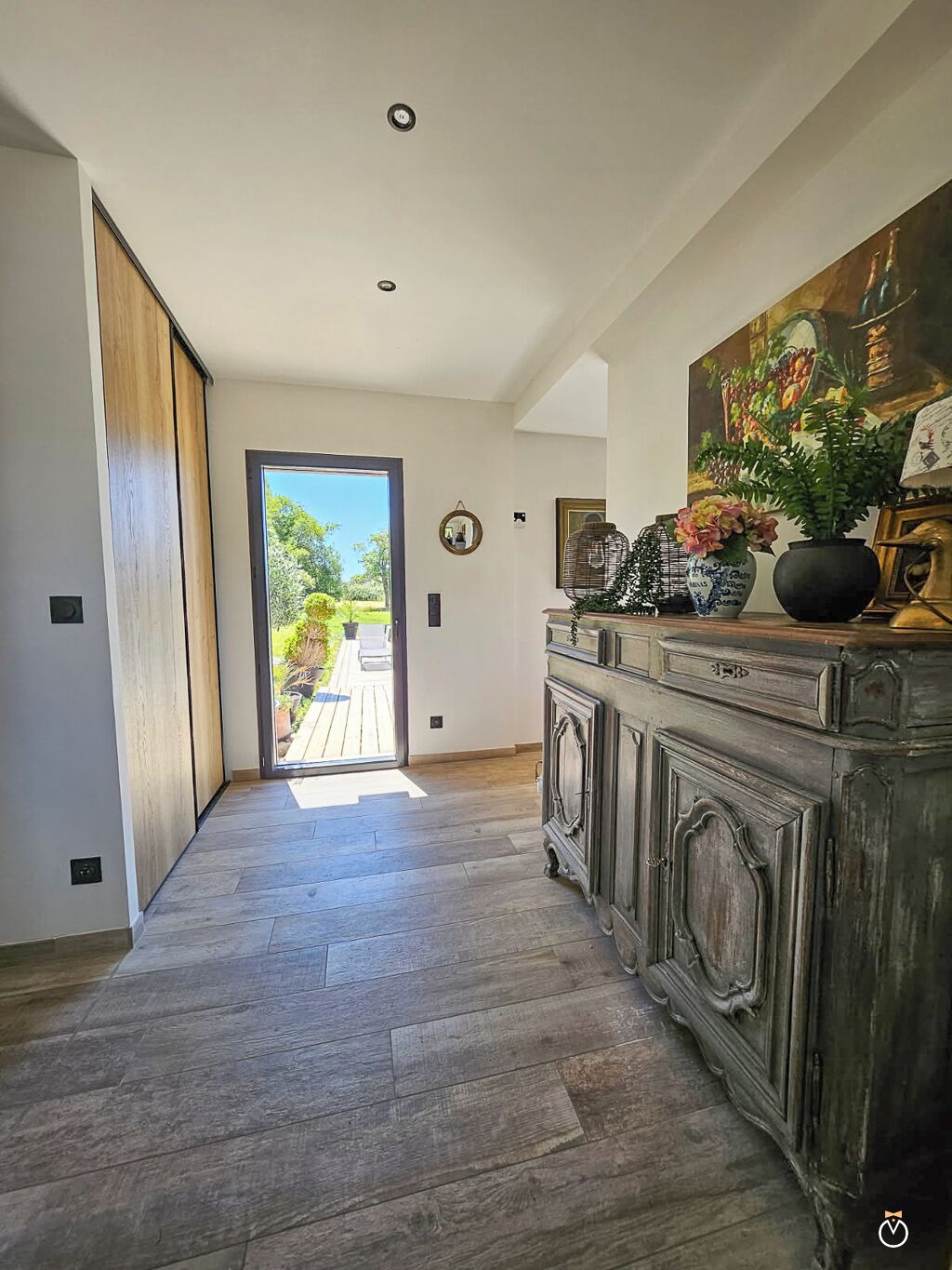 Un pasillo con piso de madera, una puerta grande de madera y un aparador con objetos decorativos.
