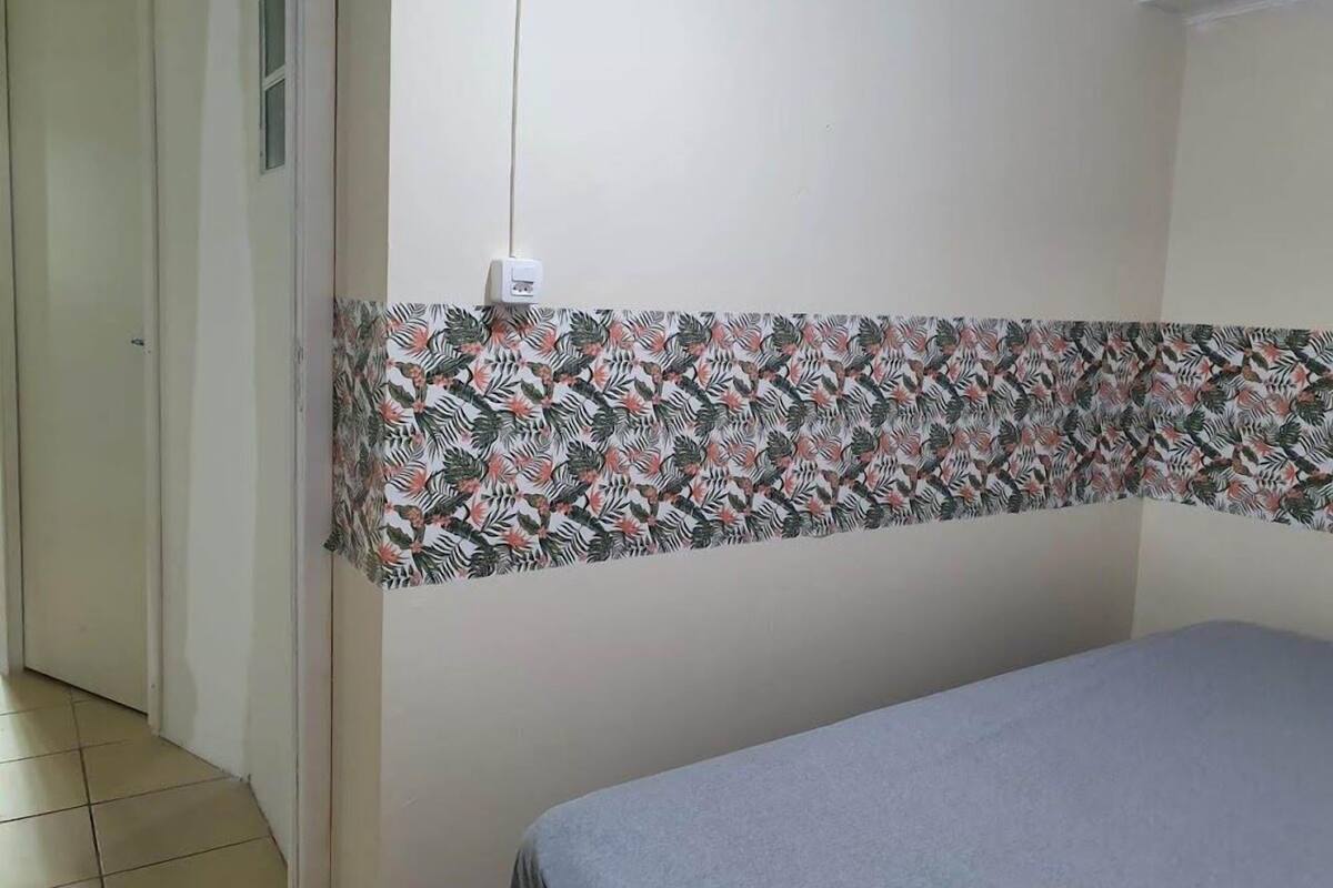 Une pièce avec un lit, un rideau à motifs, une prise de courant et une porte.