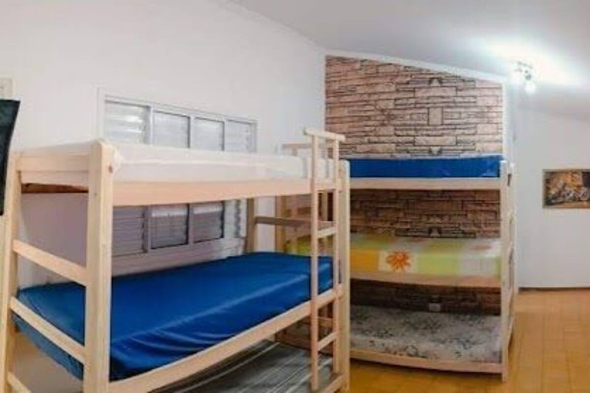 Une chambre de dortoir avec des lits superposés, un mur en pierre et une fenêtre grillagée.