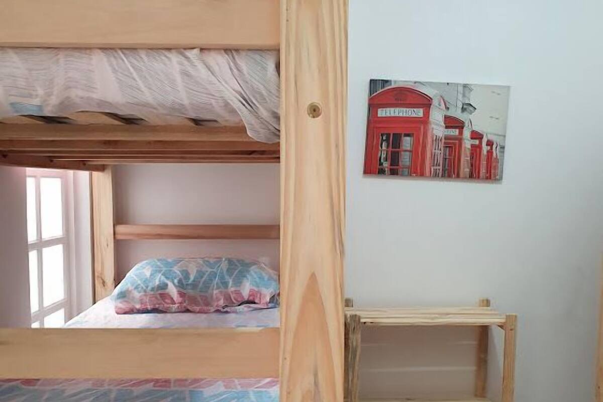 Une chambre avec des lits superposés, une tête de lit en bois, une petite étagère en bois et une affiche représentant une cabine téléphonique rouge accrochée au mur.