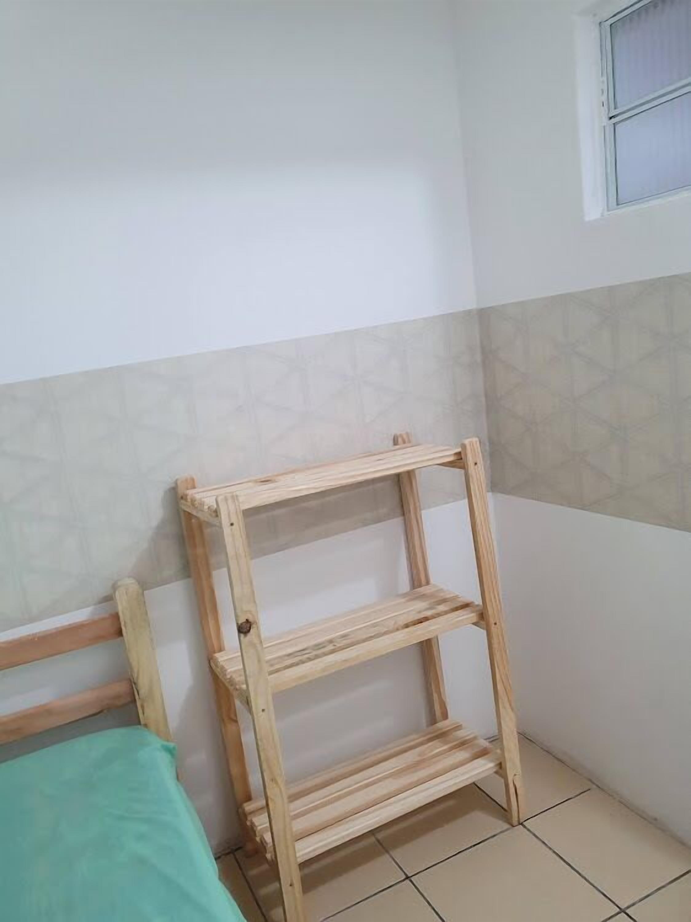A corner room with a wooden shelf unit against the wall, a bed with a green bedspread, and a window with white curtains.