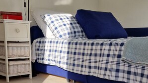Een slaapkamer met een geruit sprei, een blauw kussen, een rode vloerkleed en een witte nachtkastje met manden.