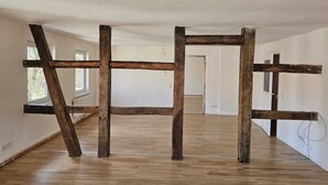 A room with exposed wooden beams, large windows, and a wooden floor. - Green apartment on the estate (Nordstemmen)