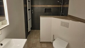 A modern bathroom with a bathtub, toilet, and shower area. - Green apartment on the estate (Nordstemmen)