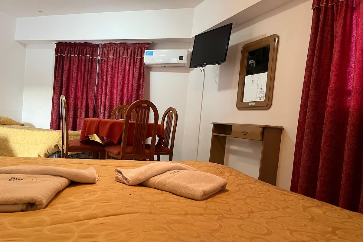 A hotel room with a bed, a desk, a chair, a television, and a window with curtains.
