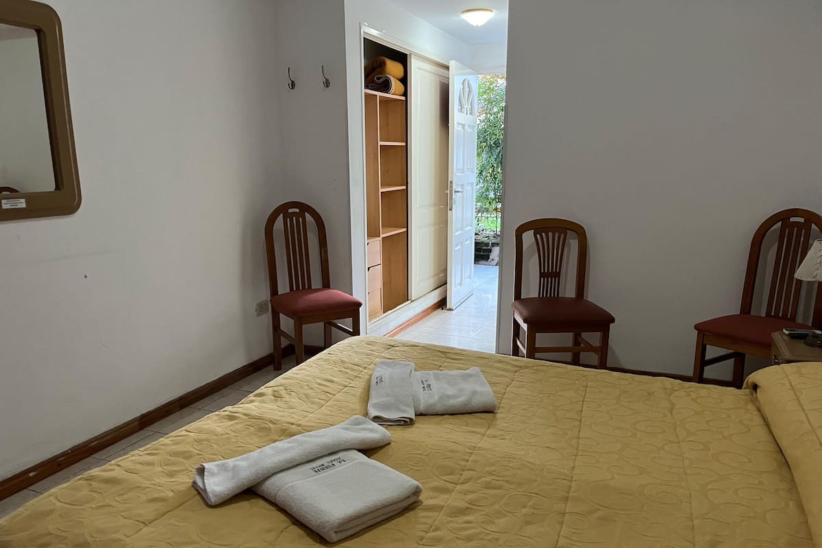 A hotel room with a bed, two wooden chairs, a wardrobe, and a mirror on the wall.