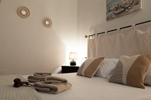 Cama bem arrumada com toalhas dobradas, abajur e uma obra de arte na parede.